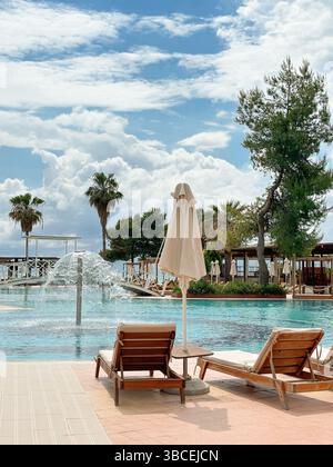 Entspannungsbereich in der Nähe des Pools mit Liegestühlen und geschlossenen Sonnenschirmen, Springbrunnen und Brücken Stockfoto