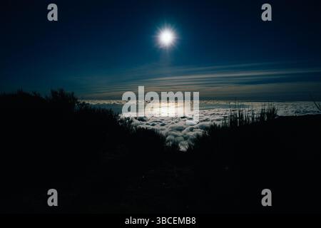 Die Sonne scheint hell über einem Wolkenmeer in der Abenddämmerung und beleuchtet den Ozean darunter Stockfoto