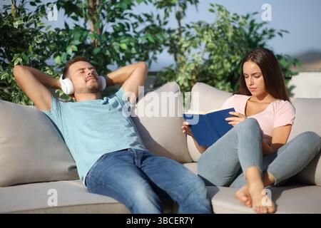 Ein Paar entspannte Zeit, die auf verschiedenen Arten Bücher lesen und Musik auf einer Terrasse hören Stockfoto