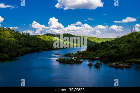 Eine atemberaubende natürliche Landschaft mit einem lebendigen, mäandernden Fluss, der durch dichte grüne Hügel unter einem dramatischen Himmel voller geschwollener weißer Wolken führt Stockfoto