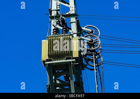 Teil eines elektrischen Posts mit einem Transformator, Isolatoren und Drähten gegen einen klaren blauen Himmel. Nahaufnahme. Stockfoto