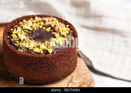 Dubai Schokoladen-Käsekuchen mit zerstoßenen Pistazienkernen auf rustikalem Strukturbrett und Stoffserviette Stockfoto