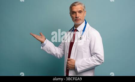 Gutaussehender Doktor Mann trägt medizinische Uniform über isoliertem Hintergrund lächelnd fröhlich präsentieren und mit Handfläche zeigen Stockfoto