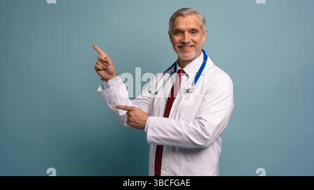 Gutaussehender Doktor Mann trägt medizinische Uniform über isoliertem Hintergrund lächelnd fröhlich präsentieren und mit Handfläche zeigen Stockfoto