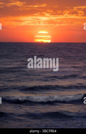Goldenes Sonnenlicht reflektiert die Oberfläche des Ozeans und schafft einen ruhigen Moment in der Abenddämmerung, der zu Frieden und Nachsicht einlädt. Stockfoto