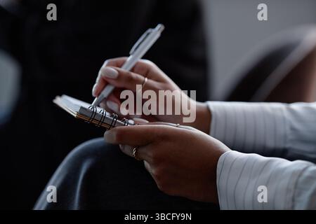 Nahaufnahme der Hände einer afroamerikanischen Frau, die während der Präsentation der Kollegen auf einer Geschäftskonferenz im Auditorium in Notizbuch schreibt, Copy Spac Stockfoto