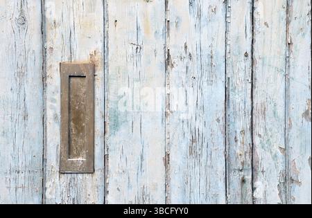 Nahaufnahme einer alten Holztür mit blauer verblassener Farbe und einem rostig geschlossenen alten Metallbriefkasten aus Messing Stockfoto