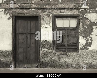 Monochromes Bild von der Vorderseite eines alten verlassenen Hauses mit verschlossenen Fenstern und verschlossenen Holztüren mit abblätternder Farbe Stockfoto
