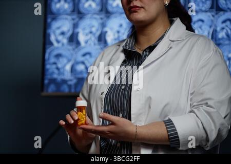 Beschnittene Aufnahme einer weiblichen Moderatorin, die eine Flasche Pillen hält, die während der Teilnahme am Neurolog orale Prüfpräparate zur Demenzbehandlung einführt Stockfoto