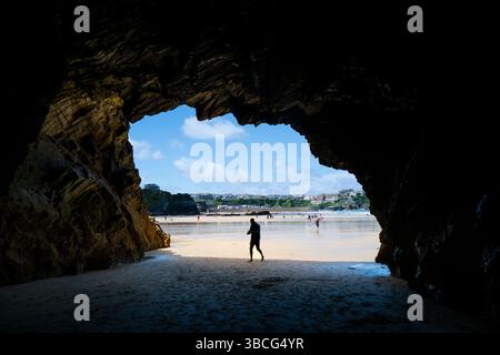 Die Figur eines männlichen Urlaubers, der eine tiefe Höhle am sonnigen GT Great Western Beach in Newquay in Cornwall in Großbritannien betritt. Stockfoto
