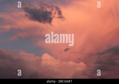 Dramatische rosa und violette Sturmwolken, die von der untergehenden Sonne beleuchtet werden und dynamische Strukturen und stimmungsvolle Atmosphäre am Abendhimmel zeigen. Stockfoto
