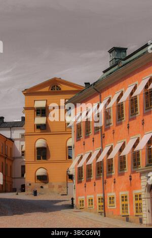 Farbenfrohe historische Gebäude mit ockerfarbenen und Terrakotta-Fassaden, Holzfenstern und klassischen Markisen im Stockholmer Altstadt. Stockfoto