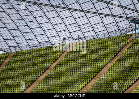 München, Deutschland. Mai 2025. Besucher des Olympiaparks spazieren unter dem Glasdach des Olympiastadions. Die Stadt München will, dass ihre Bürger über einen neuen Antrag auf Austragung der Olympischen Spiele abstimmen. Quelle: Peter Kneffel/dpa/Alamy Live News Stockfoto