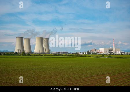 Die Kühltürme des Kernkraftwerks strahlen Dampf aus, mit grünem Feld im Vordergrund und blauem Himmel. Stockfoto