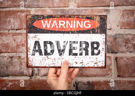 Adverb-Warnschild wird gegen Brick Wall für Grammatik-Konzept gehalten. Stockfoto