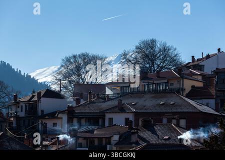 Wintermorgen in Metsovo, Griechenland, mit traditionellen Dächern und Schornsteinrauch vor der Kulisse des schneebedeckten Pindus-Berges Stockfoto
