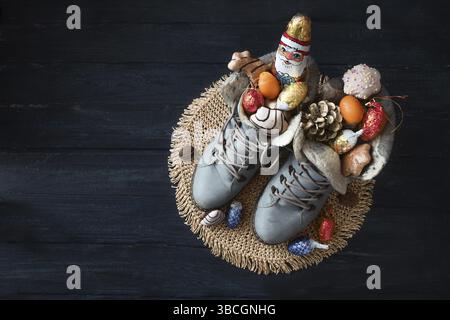 Winterstiefel gefüllt mit einem Schokoladen-Weihnachtsmann, Leckereien und Weihnachtsdekoration auf dunkelblauem Holz zum Nikolaus-Tag oder Nikolaus-Tag am 6. Dezember Stockfoto