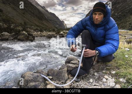 Bergsteiger filtrieren und pumpen Trinkwasser aus einem Bach in den Anden in Peru während einer Kletterexpedition in der Cordillera Blanca Stockfoto