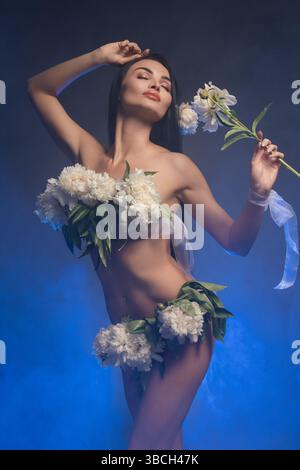 Die brünette Frau posiert anmutig mit Blumen in einer künstlerischen Umgebung Stockfoto