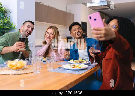 Gruppe von Freunden, die Selfie nehmen und während des Abendessens zu Hause mit Wein toasten Stockfoto