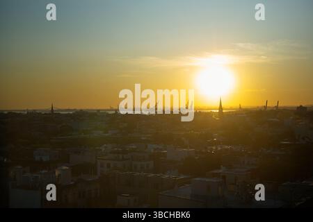 Sonnenuntergang über einer Stadtlandschaft mit Silhouetten und Kranichen unter einem goldenen Himmel. New York, USA Stockfoto