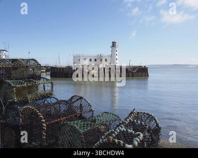 Scarborough Leuchtturm und Hafeneingang spiegeln sich in einem blauen Sommermeer mit gestapelten Hummertöpfen wider Stockfoto