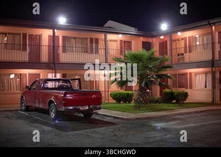 Nachtszene eines roten Pickup-Trucks, der vor einem beleuchteten Motel mit einer Palme geparkt hat. Roadtrip USA Stockfoto