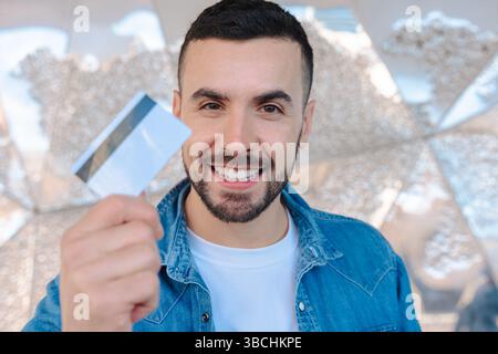 Ein lächelnder Mann mit Kreditkarte und Blick auf die Kamera in heller urbaner Umgebung Stockfoto