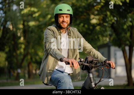 Ein lächelnder Mann fährt während des sonnigen Tages mit Helm im Park Stockfoto