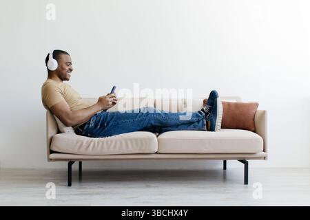 Entspannter schwarzer Mann, der Musik auf dem Smartphone mit kabellosen Kopfhörern hört Stockfoto