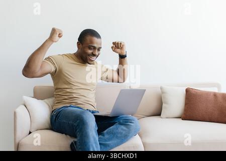Aufgeregter Afroamerikanischer Mann, Der Erfolg Bei Der Verwendung Eines Notebooks Zu Hause Feiert Stockfoto