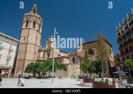 Valencia, Spanien – 12. August 2022: Seitenansicht des hoch aufragenden Glockenturms der Kathedrale von Valencia und der prunkvollen Barockfassade mit Blick auf die Turia-Gärten unter einer de Stockfoto