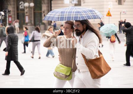 Belgrad, Serbien - 17. Mai 2025: Elegantes miteinander verbundenes Paar, das im Frühlingsregen der Stadt unter einem Regenschirm zusammenläuft Stockfoto