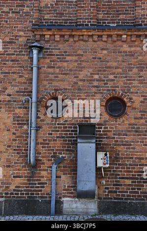 Ziegelwand einer alten Fabrik mit runden Fenstern und Lüftungsrohren Stockfoto