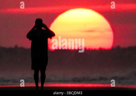 Isle Of Palms, Usa. Mai 2025. Ein Mann, der vom Sonnenaufgang umrahmt wird, macht ein Foto, während die Sonne am Front Beach am 20. Mai 2025 in Isle of Palms, South Carolina, über den Horizont steigt. Quelle: Richard Ellis/Richard Ellis/Alamy Live News Stockfoto