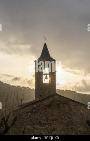 Eine massive Bergkirche aus Stein mit Kirchturm und Sonne Stern, der im Winter unter einem bewölkten Himmel durchscheint Abend Stockfoto