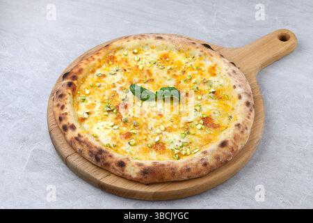 Weiße Gourmet-Pizza mit geschmolzenem Käse, Honig gehackten Pistazien und frischem Basilikum auf einem rustikalen Holzbrett. Stockfoto