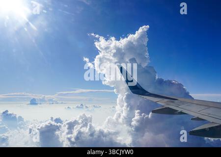 Hoch über den Wolken, Ein atemberaubender Blick aus der Luft von einem Flugzeugfenster mit hoch aufragenden Cumulus Wolken, der den Flugzeugflügel zeigt, atemberaubende Aussicht Stockfoto