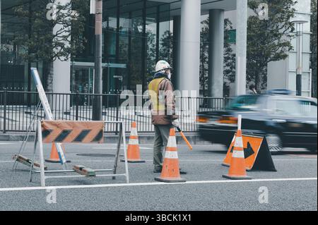 Die Verkehrswache steht im Zentrum von Tokio, während Autos an einer verbarrikadierten Spur vorbeifahren Stockfoto