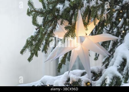 Beleuchteter weißer Mährischer Stern hängt in einer schneebedeckten Weihnachtstanne als festliche Weihnachtsdekoration, Kopierraum, sele Stockfoto