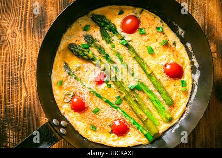 Spargel mit Rührei und Kirschtomaten in einer Pfanne auf hölzernem Hintergrund. Blick von oben. Leerzeichen für Text. Hochwertige Fotos Stockfoto