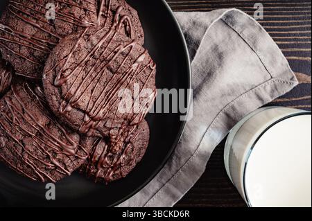 Close-up von Teller mit dreifacher Schokolade Kirschkekse mit Glas Milch: Schokoladenkirschkekse auf einem Teller mit einer Tasse Milch Stockfoto