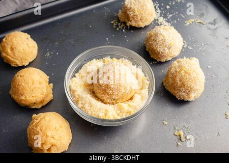 Kuchenteig mit Zitronenzucker überzogen: Nahaufnahme einer Backform mit ein paar Kugeln Zucker-Keks-Teig Stockfoto