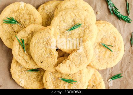 Rosmarin-Lemon Sugar Cookies, gestapelt auf braunem Geschenkpapier: Direkt über Zuckerkeksen und verstreuten Rosmarinblättern auf braunem Papier Stockfoto