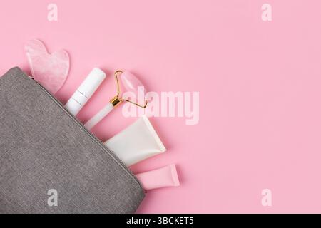 Set von Kosmetik für Gesichtspflege von Tube von Creme, Gel und Massagegeräte Jaderolle, guasha in grauer Kosmetiktasche auf rosa Hintergrund. Massagegeräte für das Gesicht. Anti-Age-, Lifting- und straffende Pflege. Modernes Selbstpflegekonzept. Stockfoto