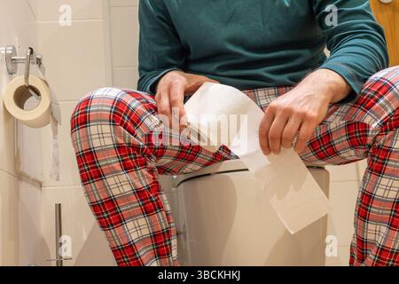 Person im Pyjama, die auf der Toilette sitzt, mit Toilettenpapier in der Hand. Durchfall, Magenschmerzen. Gesundheitskonzept Stockfoto