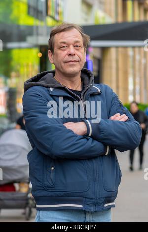 Ein selbstbewusster Mann mittleren Alters posiert an einem Frühlingstag in lässiger Kleidung auf einer Straße der Stadt Stockfoto