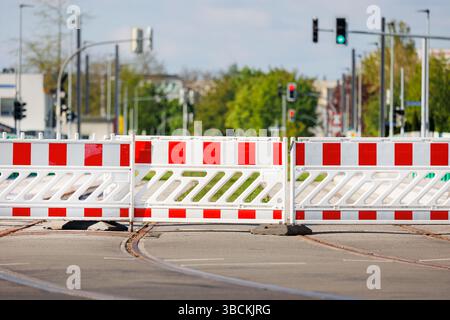 Temporäre rot-weiße Verkehrsbarrikaden blockieren den Zugang zu Straßenbahnschienen auf der deutschen Stadtstraße. Der Hintergrund zeigt Ampeln, Bäume und verschwommene Städte Stockfoto