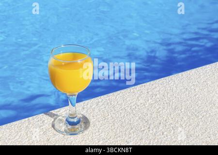 Glas gefüllt mit Orangensaft stehen am Rand des blauen Swimmingpool Stockfoto