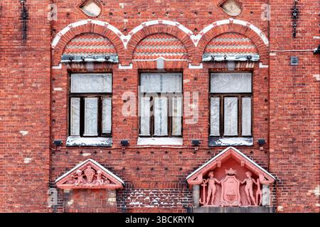 Drei rechteckige Fenster mit braunen Rahmen und gebogenem Gesims gegen eine rote Backsteinmauer. Aus den Fenstern der World Series. Stockfoto